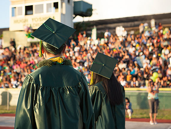 Two graduates facing the crowd